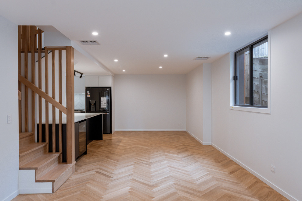 Large modern u-shaped kitchen pantry in Brisbane with an undermount sink, blue cabinets, marble benchtops, white splashback, stone tile splashback, black appliances, light hardwood floors, with island, brown floor and white benchtop.