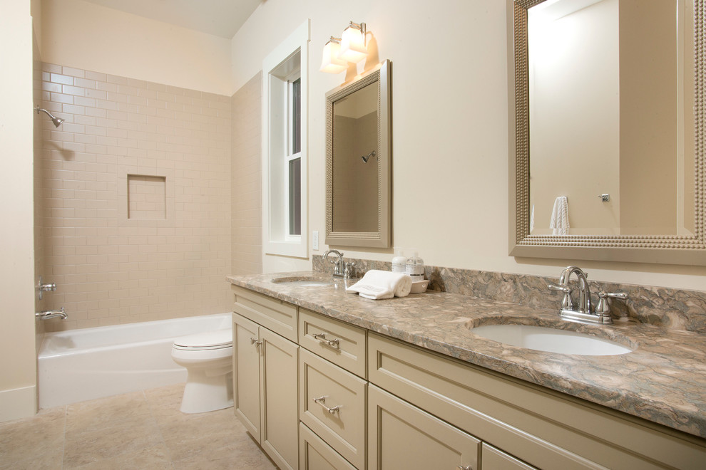 Photo of a mid-sized traditional bathroom in Charleston with an undermount sink, recessed-panel cabinets, grey cabinets, limestone benchtops, a drop-in tub, a shower/bathtub combo, a two-piece toilet, beige tile, ceramic tile, white walls and ceramic floors.