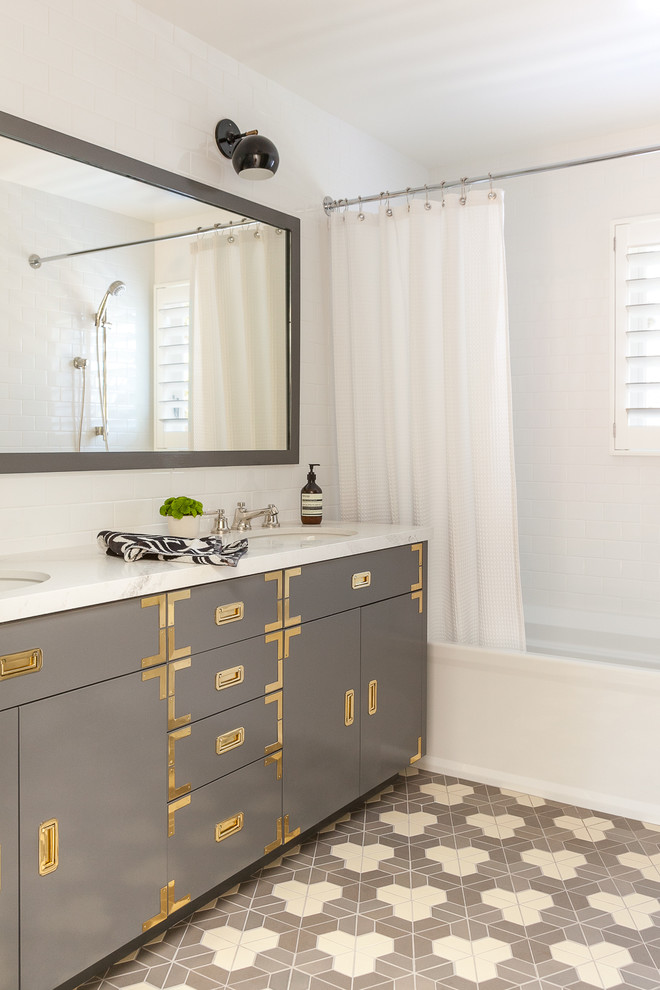 Photo of a mid-sized transitional kids bathroom in San Francisco with grey cabinets, an alcove tub, a shower/bathtub combo, white tile, ceramic tile, ceramic floors, an undermount sink, quartzite benchtops, a shower curtain, white benchtops, flat-panel cabinets, white walls and multi-coloured floor.