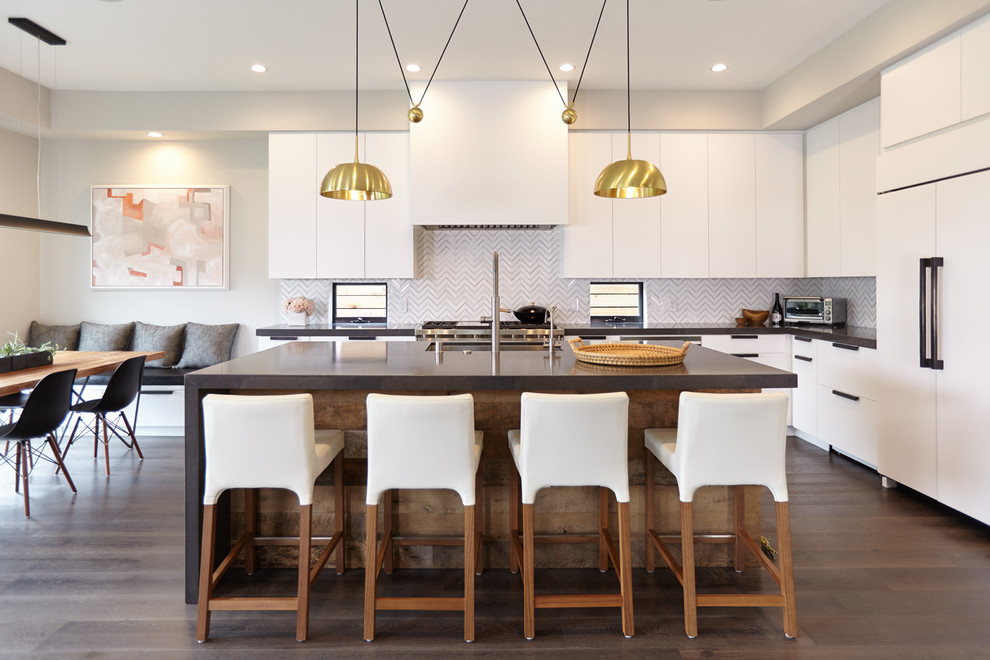 This is an example of a contemporary l-shaped eat-in kitchen in Los Angeles with an undermount sink, flat-panel cabinets, white cabinets, white splashback, stainless steel appliances, dark hardwood floors and with island.