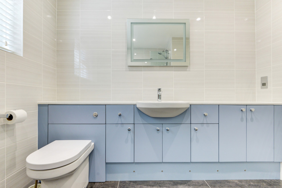 Aménagement d'une salle de bain grise et blanche contemporaine de taille moyenne pour enfant avec un placard à porte plane, des portes de placard bleues, une baignoire en alcôve, un combiné douche/baignoire, WC suspendus, un carrelage beige, des carreaux de céramique, un mur beige, un lavabo intégré, un plan de toilette en stratifié, un sol gris, un plan de toilette blanc, meuble simple vasque et meuble-lavabo encastré.