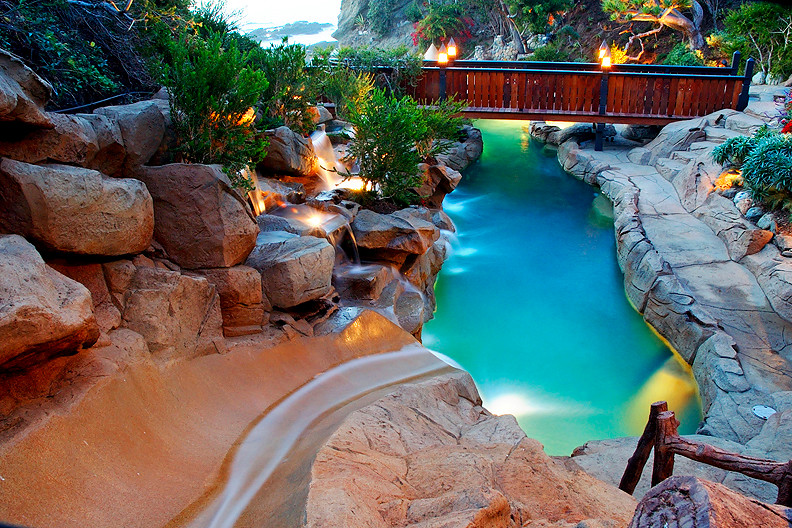 Photo of an expansive tropical backyard custom-shaped pool in Orange County with a water slide and stamped concrete.