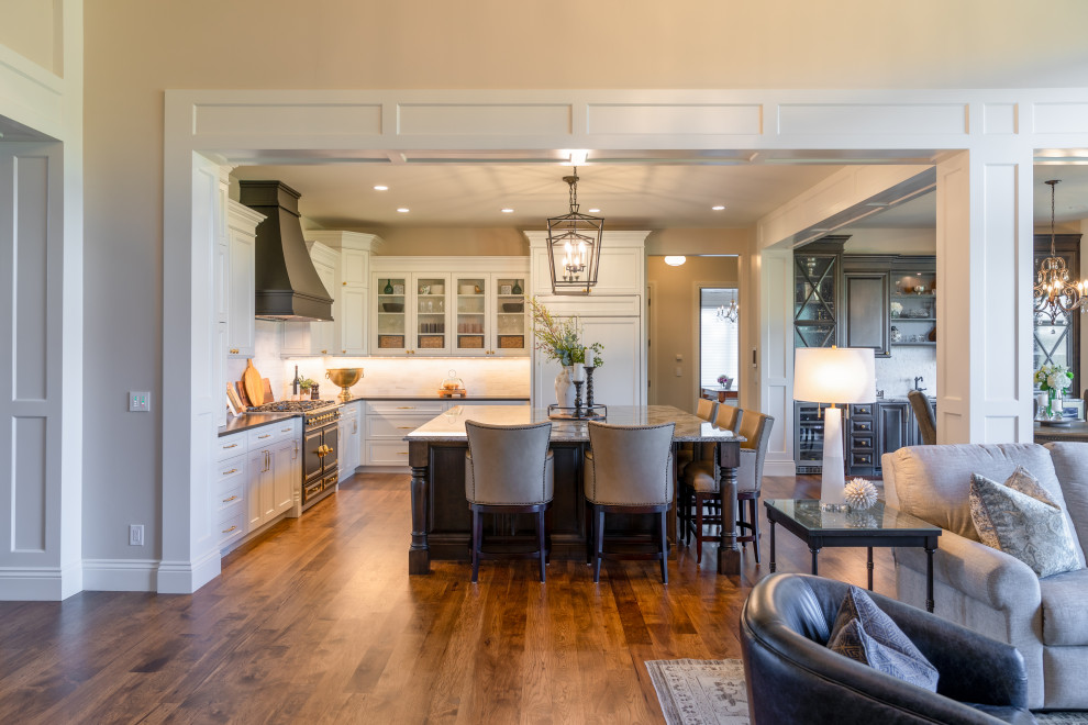 Elegant l-shaped medium tone wood floor and multicolored floor open concept kitchen photo in Denver with recessed-panel cabinets, white cabinets, white backsplash, stone tile backsplash, paneled appliances, an island and black countertops