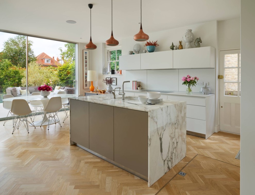 Photo of a large contemporary l-shaped eat-in kitchen in London with a double-bowl sink, flat-panel cabinets, grey cabinets, solid surface benchtops, light hardwood floors, with island, beige floor and grey benchtop.