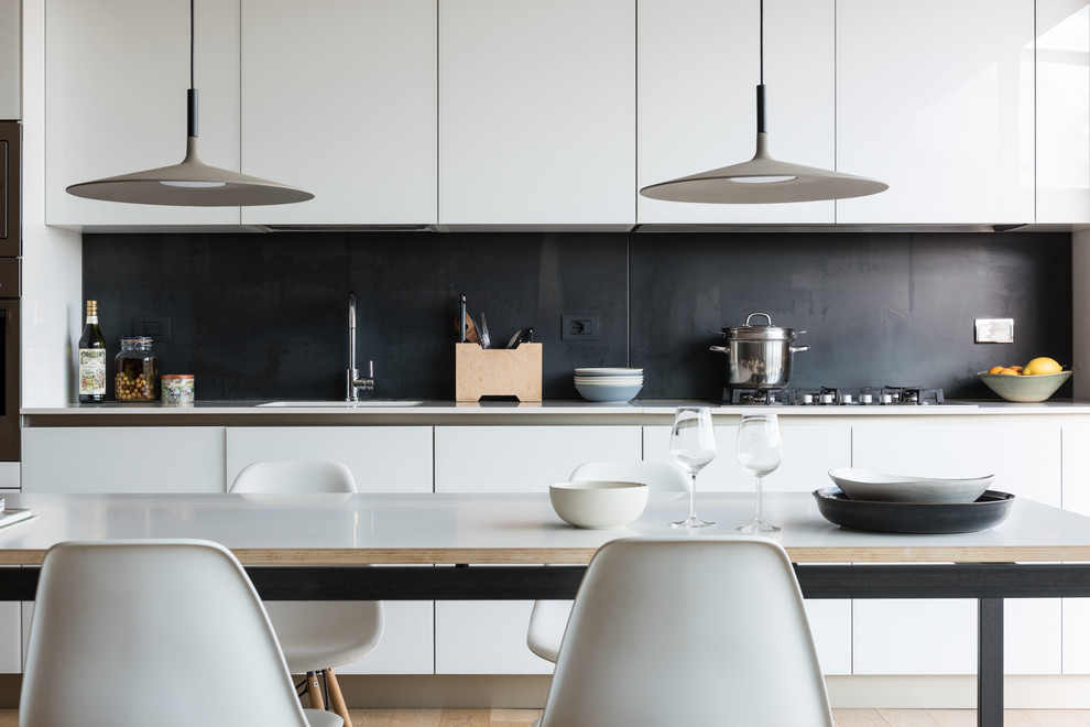 Photo of a modern single-wall eat-in kitchen in Rome with an integrated sink, flat-panel cabinets, white cabinets, quartzite benchtops, black splashback, slate splashback, white appliances, light hardwood floors and white benchtop.