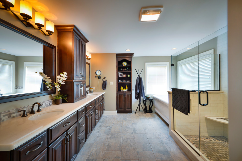 Photo of a large transitional master bathroom in Other with an undermount sink, beaded inset cabinets, dark wood cabinets, quartzite benchtops, a freestanding tub, an alcove shower, a two-piece toilet, multi-coloured tile, glass sheet wall, beige walls and porcelain floors.