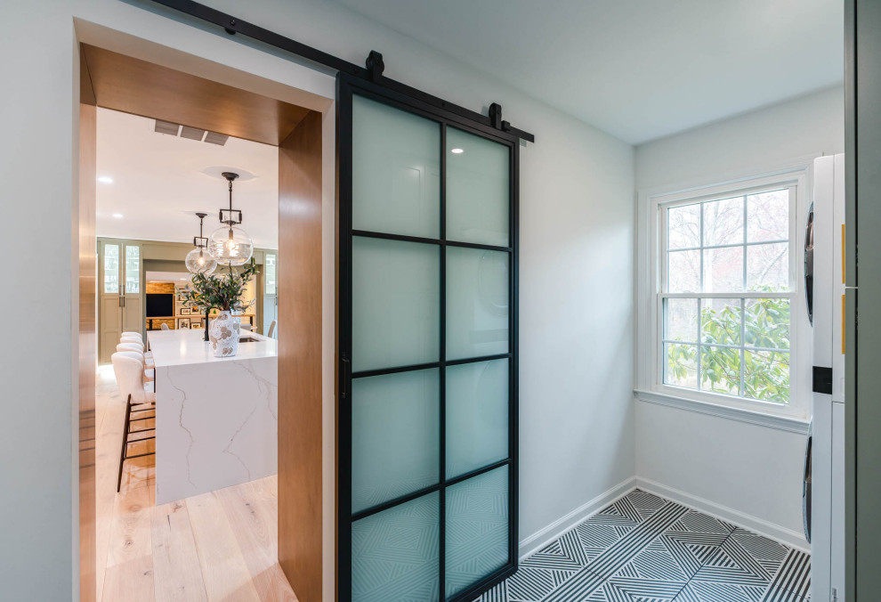 Small traditional galley utility room in DC Metro with shaker cabinets, green cabinets, white walls, porcelain flooring, a stacked washer and dryer and black floors.
