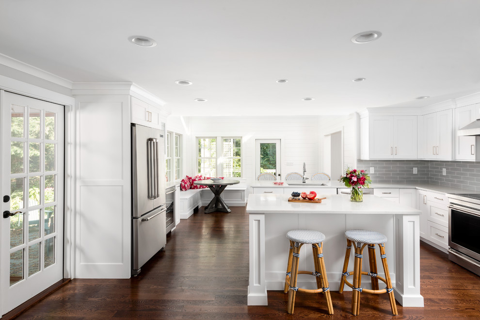 This is an example of a mid-sized traditional l-shaped eat-in kitchen in Boston with an undermount sink, shaker cabinets, white cabinets, quartzite benchtops, grey splashback, subway tile splashback, stainless steel appliances, medium hardwood floors, multiple islands and brown floor.