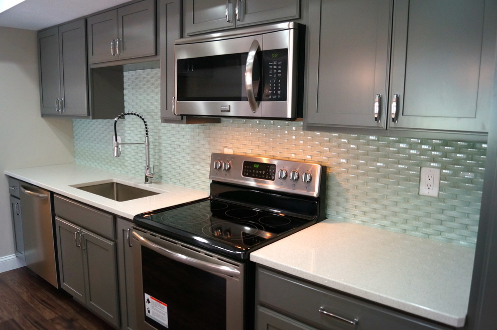 Inspiration for a mid-sized modern galley medium tone wood floor kitchen pantry remodel in Cleveland with a single-bowl sink, shaker cabinets, gray cabinets, quartz countertops, green backsplash, glass sheet backsplash, stainless steel appliances and an island