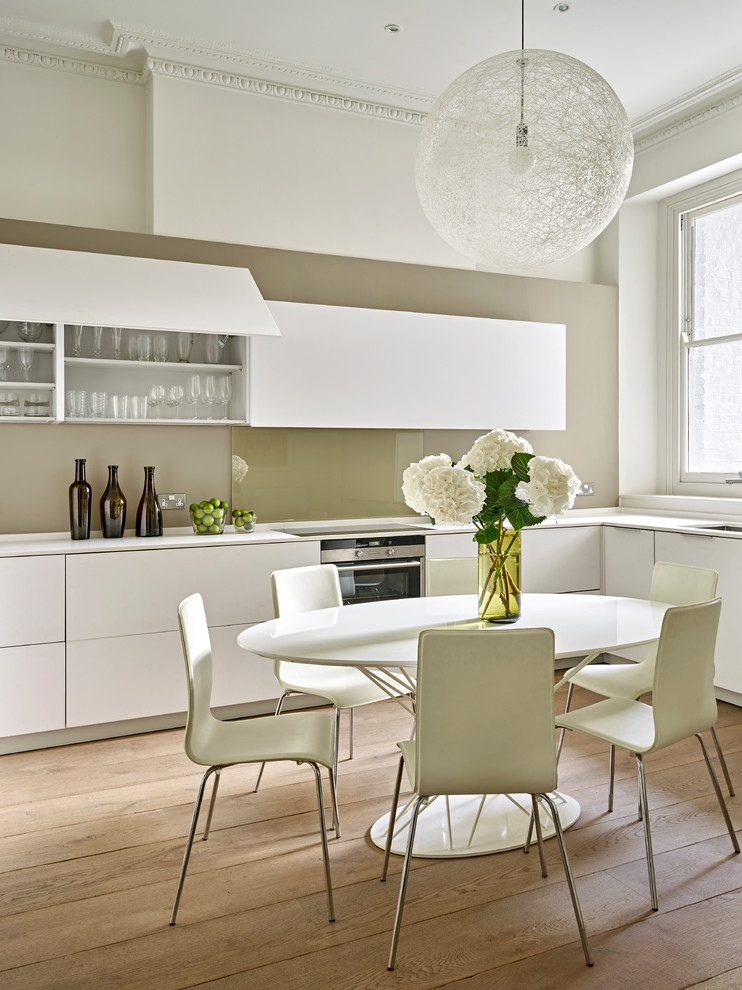 Design ideas for a mid-sized contemporary l-shaped eat-in kitchen in London with a single-bowl sink, flat-panel cabinets, white cabinets, solid surface benchtops, glass sheet splashback, stainless steel appliances, medium hardwood floors and no island.