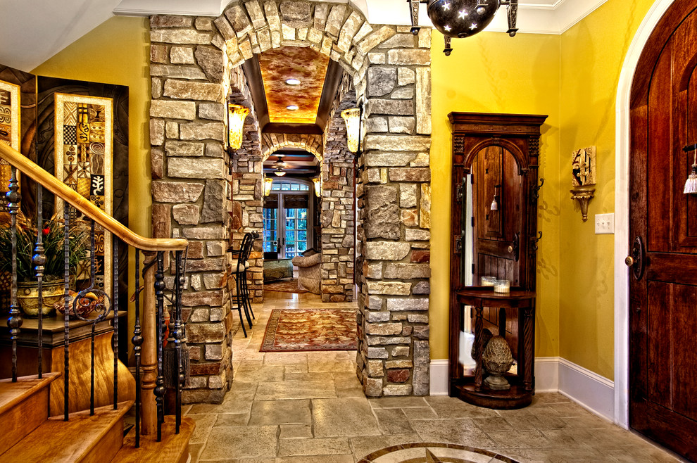 This is an example of a large mediterranean foyer in Miami with yellow walls, travertine floors, a single front door and a dark wood front door.