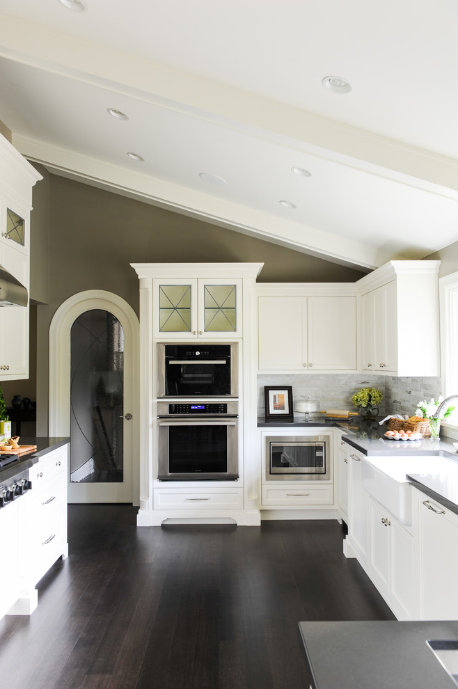 Inspiration for a large transitional u-shaped dark wood floor eat-in kitchen remodel in Vancouver with a farmhouse sink, recessed-panel cabinets, white cabinets, glass countertops, white backsplash, stainless steel appliances and no island