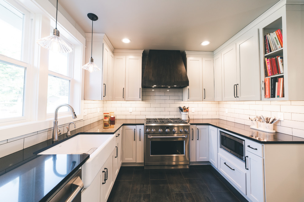 Photo of a large country u-shaped kitchen in Seattle with a farmhouse sink, shaker cabinets, white cabinets, quartz benchtops, white splashback, subway tile splashback, stainless steel appliances, black floor and black benchtop.