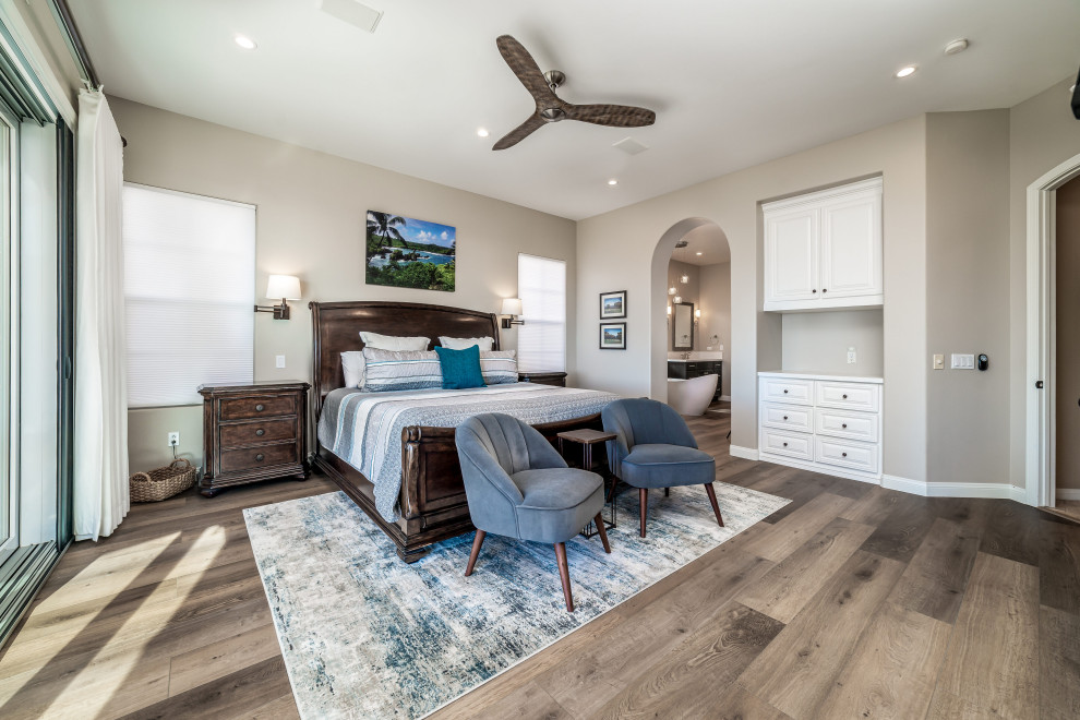 Mid-sized beach style master bedroom in San Diego with beige walls, vinyl floors, a standard fireplace, a stone fireplace surround and brown floor.