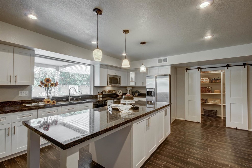 This is an example of a large country l-shaped kitchen pantry in Phoenix with a double-bowl sink, shaker cabinets, white cabinets, granite benchtops, black splashback, stone slab splashback, stainless steel appliances, porcelain floors and with island.