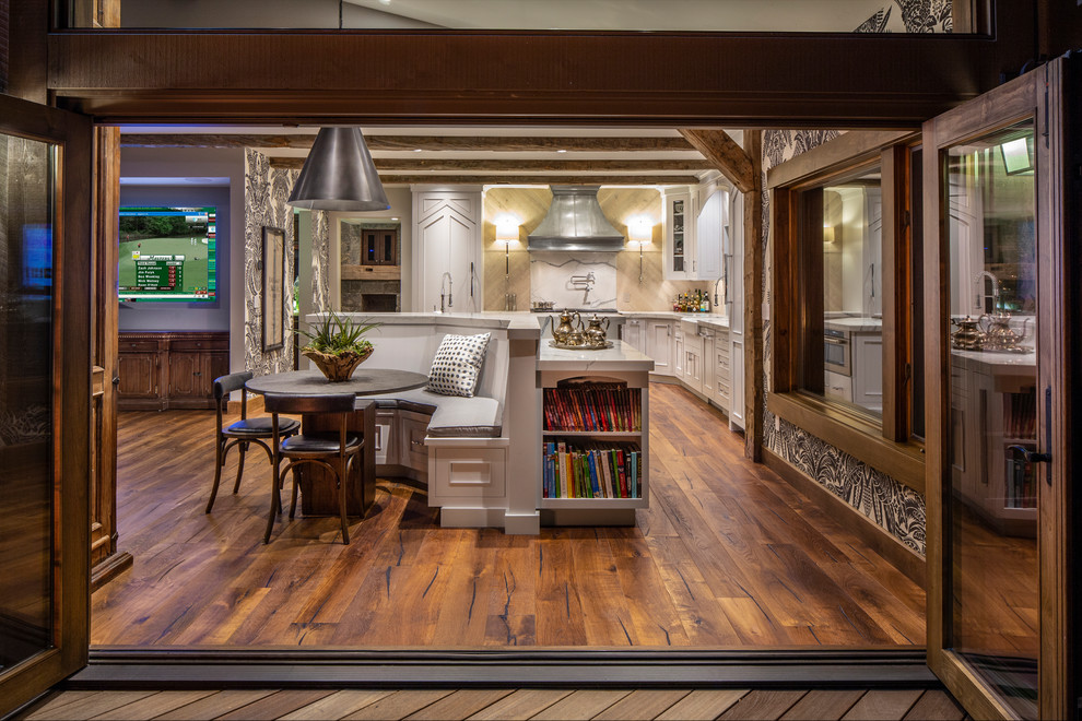 Example of a large mountain style l-shaped medium tone wood floor and brown floor eat-in kitchen design with a farmhouse sink, recessed-panel cabinets, white cabinets, quartz countertops, beige backsplash, wood backsplash, paneled appliances, two islands and white countertops