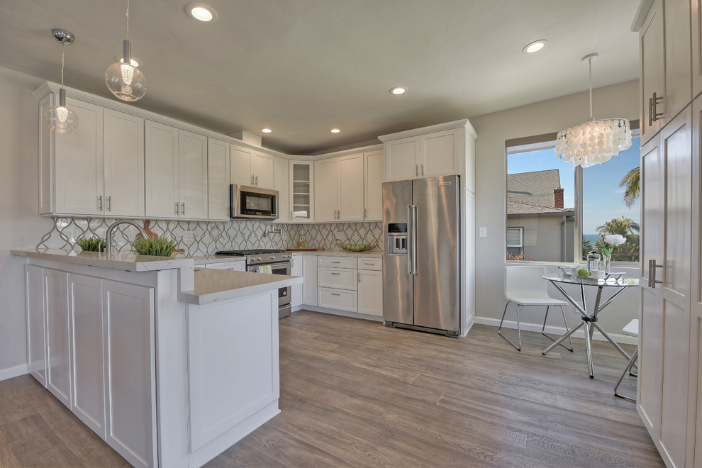 This is an example of a mid-sized contemporary u-shaped open plan kitchen in San Diego with an undermount sink, shaker cabinets, yellow cabinets, quartzite benchtops, grey splashback, stone tile splashback, stainless steel appliances, light hardwood floors, no island, grey floor and white benchtop.