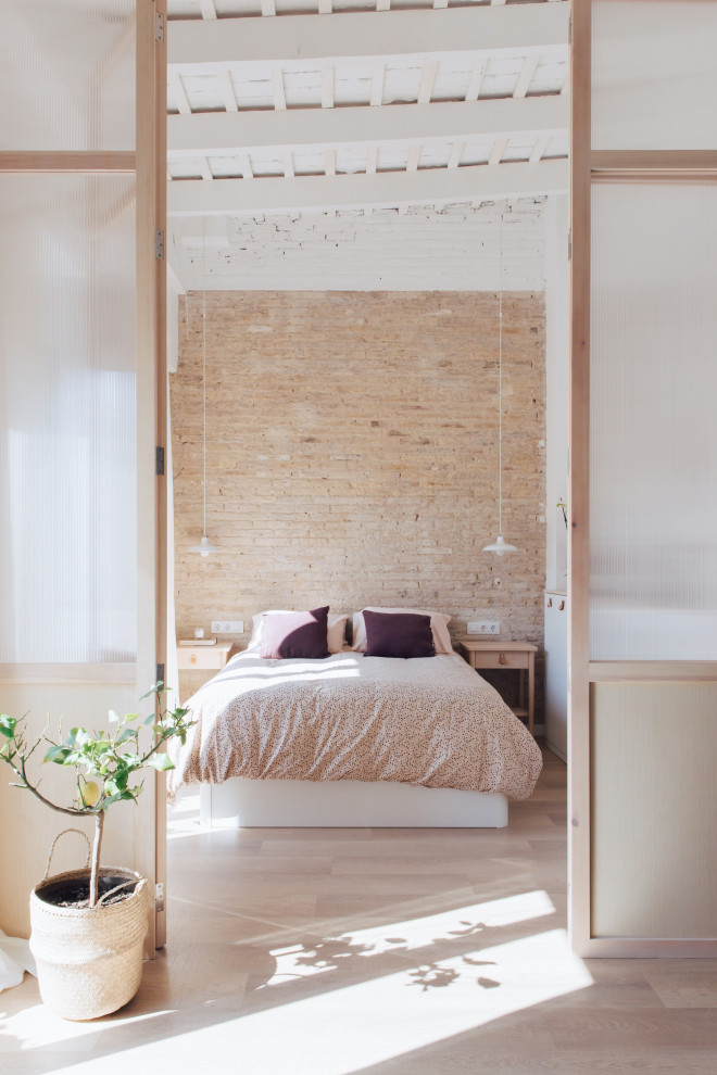 Esempio di una piccola camera matrimoniale industriale con pareti bianche, pavimento in laminato, travi a vista e pareti in mattoni
