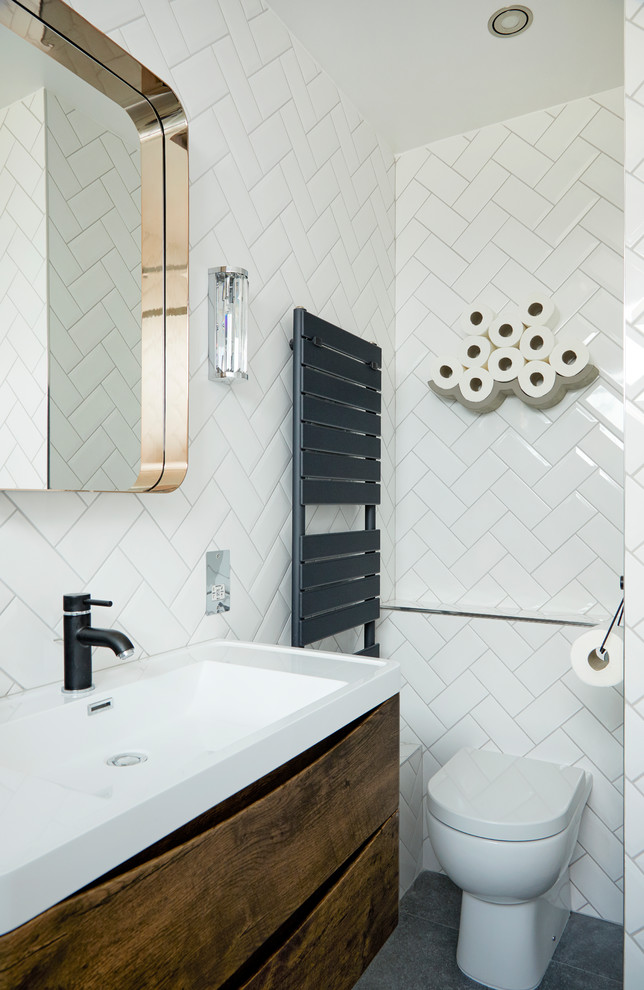 This is an example of a small midcentury master bathroom in London with flat-panel cabinets, brown cabinets, a one-piece toilet, white tile, subway tile, white walls, a wall-mount sink, grey floor, cement tiles and solid surface benchtops.