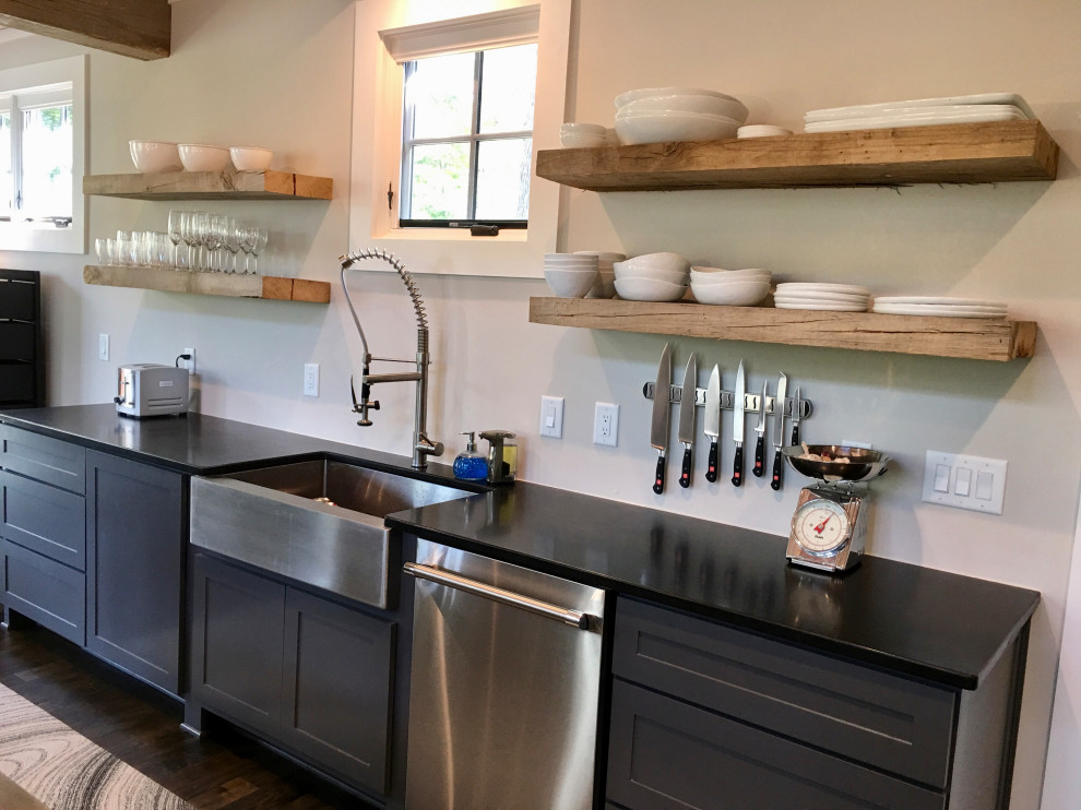 Design ideas for a mid-sized industrial l-shaped open plan kitchen in Raleigh with a farmhouse sink, shaker cabinets, grey cabinets, quartz benchtops, stainless steel appliances, dark hardwood floors, a peninsula, brown floor and black benchtop.