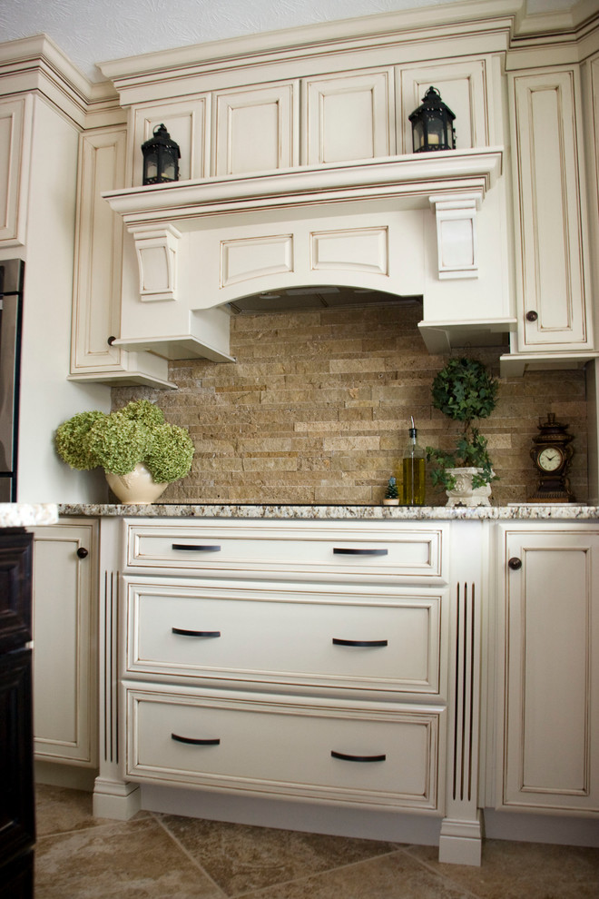 Example of a large u-shaped ceramic tile eat-in kitchen design with a farmhouse sink, recessed-panel cabinets, distressed cabinets, granite countertops, beige backsplash, stone tile backsplash, stainless steel appliances and an island