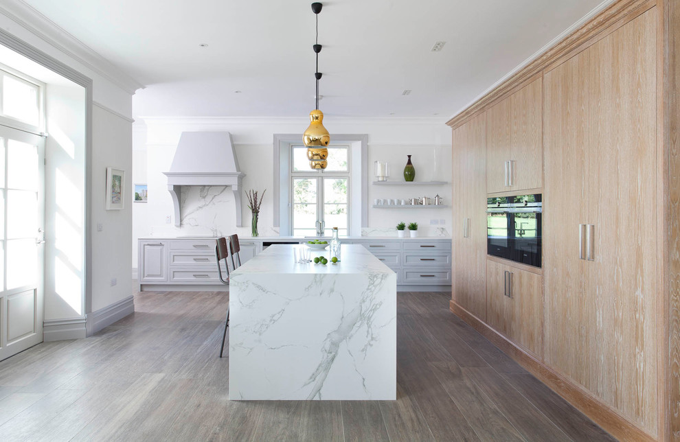 Large contemporary u-shaped open plan kitchen in Other with an undermount sink, raised-panel cabinets, grey cabinets, quartz benchtops, white splashback, stone slab splashback, black appliances, porcelain floors, with island and brown floor.