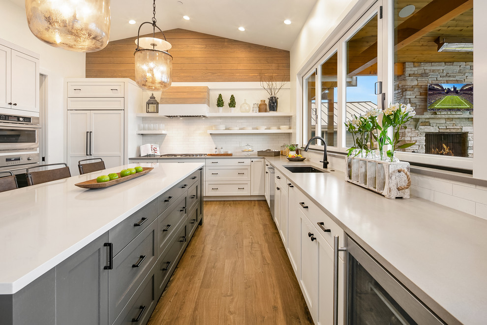 Inspiration for a beach style l-shaped kitchen in Seattle with an undermount sink, shaker cabinets, white cabinets, white splashback, subway tile splashback, medium hardwood floors, with island, grey benchtop and panelled appliances.