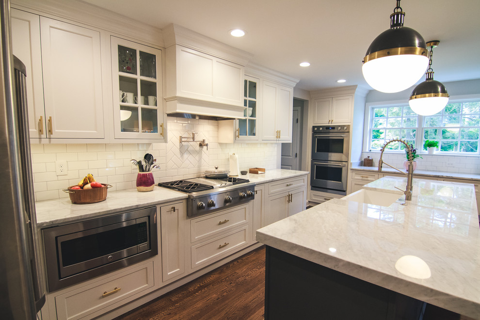 Design ideas for a large traditional u-shaped open plan kitchen in Baltimore with a farmhouse sink, shaker cabinets, white cabinets, marble benchtops, white splashback, subway tile splashback, stainless steel appliances, medium hardwood floors, with island and brown floor.