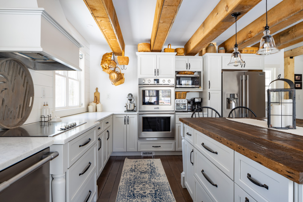 Photo of a large country l-shaped eat-in kitchen in Portland Maine with a farmhouse sink, shaker cabinets, grey cabinets, marble benchtops, white splashback, shiplap splashback, stainless steel appliances, dark hardwood floors, with island, brown floor, white benchtop and exposed beam.
