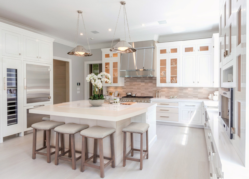 Large beach style kitchen in Other with a farmhouse sink, white cabinets, beige splashback, stainless steel appliances, light hardwood floors, with island, glass-front cabinets, matchstick tile splashback and beige floor.