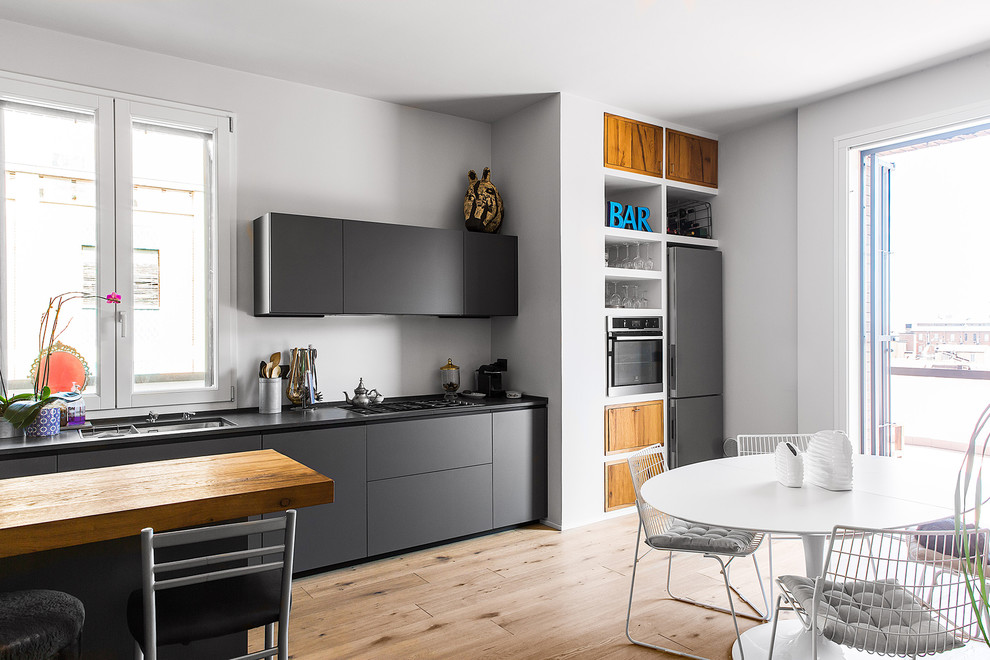Large scandinavian eat-in kitchen in Bologna with flat-panel cabinets, stainless steel appliances, light hardwood floors, an undermount sink, black cabinets, beige floor and black benchtop.