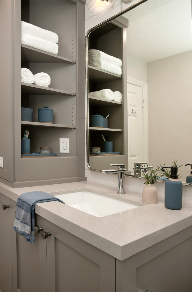 Photo of a mid-sized beach style bathroom in Orange County with shaker cabinets, grey cabinets, an alcove shower, a one-piece toilet, white tile, ceramic tile, white walls, porcelain floors, an undermount sink, engineered quartz benchtops, grey floor, a hinged shower door, beige benchtops, a niche, a single vanity and a built-in vanity.