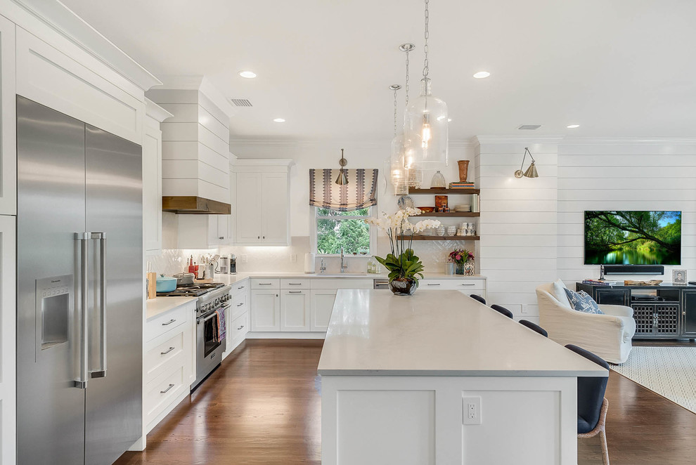 Photo of a large transitional l-shaped open plan kitchen in Orlando with an undermount sink, shaker cabinets, white cabinets, white splashback, stainless steel appliances, medium hardwood floors, with island, brown floor, marble benchtops and ceramic splashback.