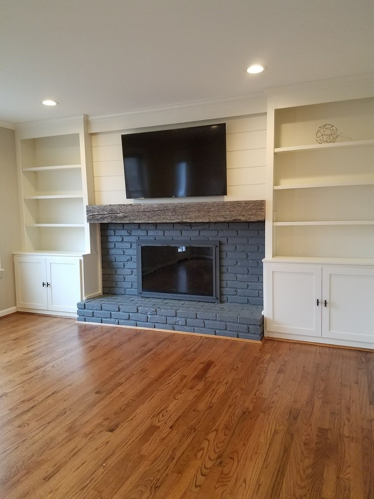 This is an example of a large transitional enclosed family room in Cincinnati with grey walls, medium hardwood floors, a standard fireplace, a brick fireplace surround, a wall-mounted tv and brown floor.