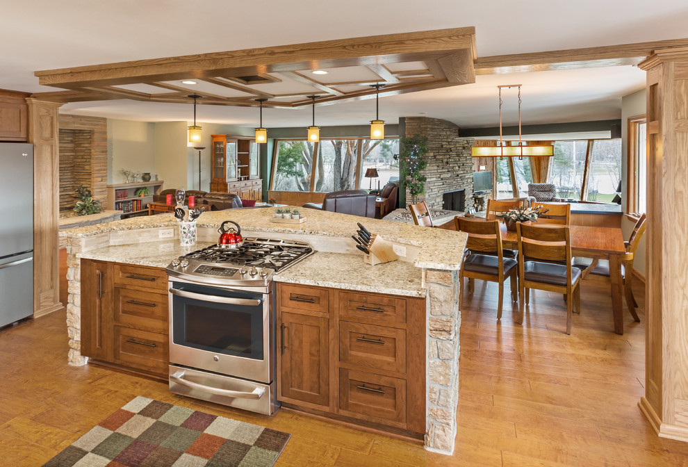 Design ideas for a large traditional eat-in kitchen in Milwaukee with an undermount sink, recessed-panel cabinets, medium wood cabinets, granite benchtops, beige splashback, stone tile splashback, stainless steel appliances, medium hardwood floors, with island and brown floor.