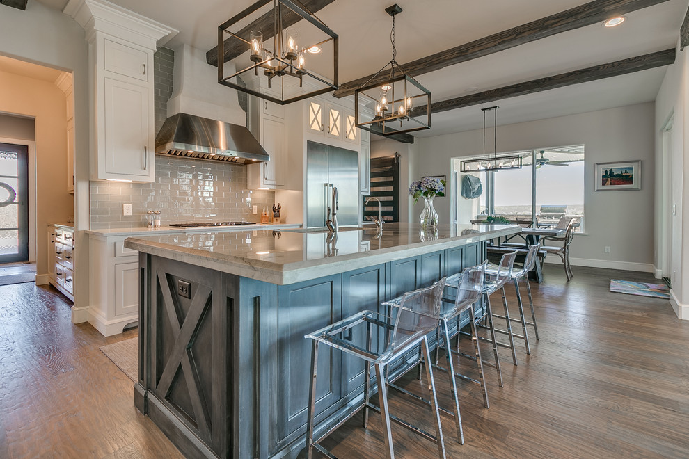Photo of an expansive country l-shaped eat-in kitchen in Oklahoma City with a farmhouse sink, shaker cabinets, white cabinets, quartz benchtops, grey splashback, subway tile splashback, stainless steel appliances, light hardwood floors, with island and grey floor.