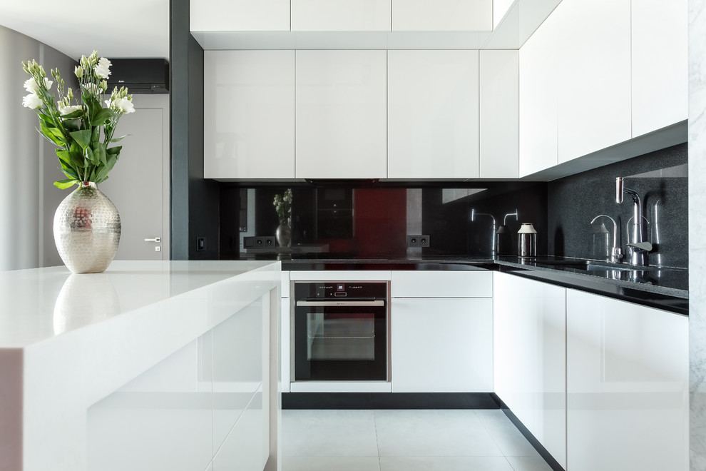 Inspiration for a small contemporary l-shaped open plan kitchen in Moscow with an undermount sink, flat-panel cabinets, white cabinets, black splashback, white appliances, porcelain floors, with island, white floor and black benchtop.