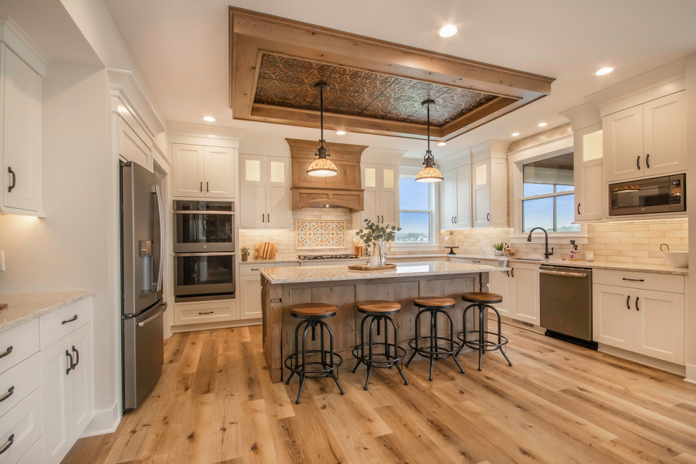 Photo of a transitional u-shaped open plan kitchen in Grand Rapids with shaker cabinets, white cabinets, wood benchtops, stone tile splashback, stainless steel appliances, vinyl floors, with island and white benchtop.