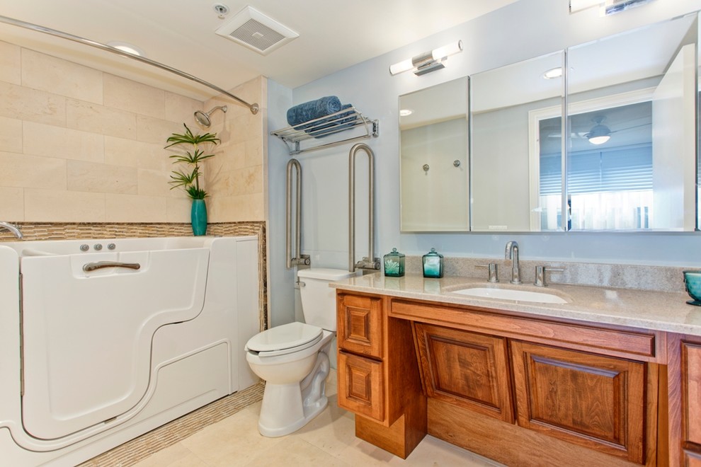 Photo of a mid-sized transitional master bathroom in San Diego with raised-panel cabinets, medium wood cabinets, a two-piece toilet, an undermount sink, engineered quartz benchtops, a freestanding tub, a shower/bathtub combo, beige tile, stone tile, grey walls and travertine floors.