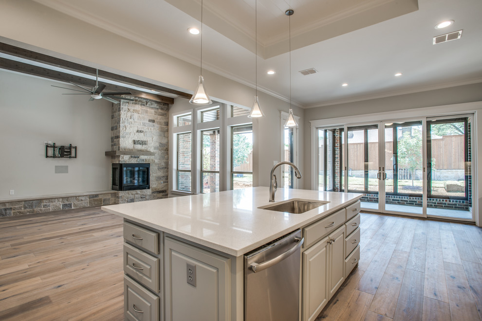 Large transitional l-shaped open plan kitchen in Dallas with an undermount sink, raised-panel cabinets, grey cabinets, stainless steel appliances, plywood floors and with island.