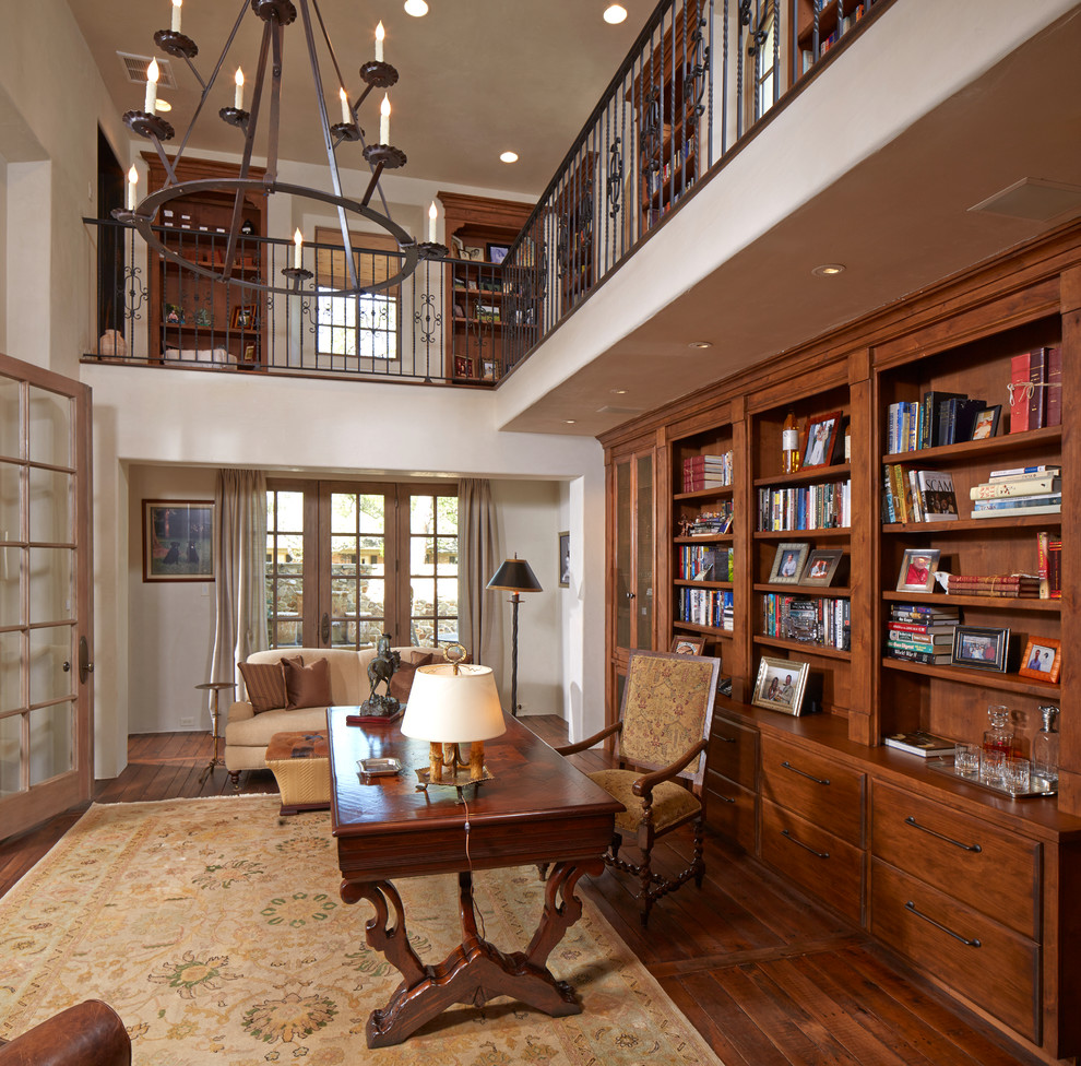 Inspiration for a large mediterranean home office in Houston with white walls, dark hardwood floors, a freestanding desk, brown floor, a library and no fireplace.