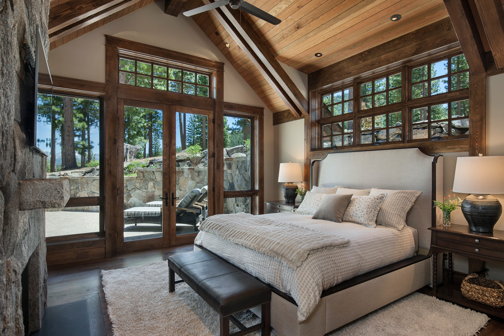 This is an example of a mid-sized country guest bedroom in Sacramento with beige walls, dark hardwood floors, a standard fireplace, a stone fireplace surround and brown floor.