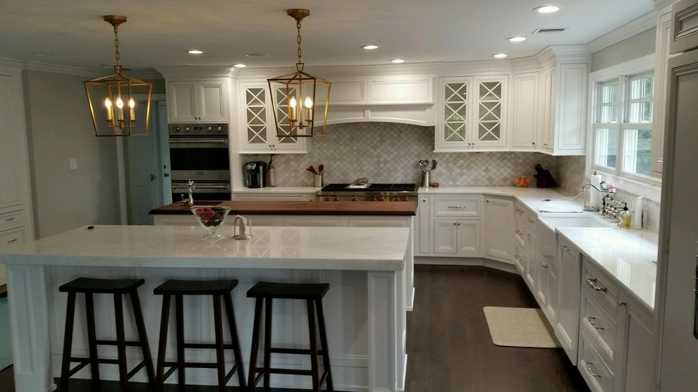 Huge transitional l-shaped dark wood floor eat-in kitchen photo in New York with a farmhouse sink, shaker cabinets, white cabinets, marble countertops, white backsplash, porcelain backsplash, stainless steel appliances and two islands