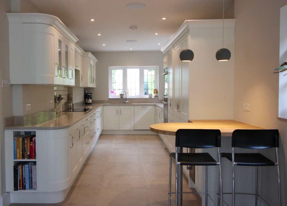 This is an example of a mid-sized contemporary galley eat-in kitchen in Buckinghamshire with shaker cabinets, white cabinets, quartzite benchtops, ceramic splashback, porcelain floors, a peninsula, an integrated sink, white splashback and black appliances.