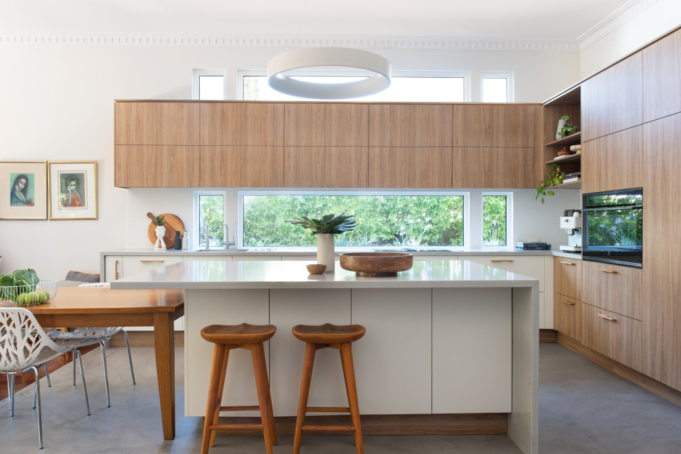 Inspiration for a mid-sized contemporary l-shaped eat-in kitchen in Perth with a drop-in sink, flat-panel cabinets, medium wood cabinets, quartz benchtops, white splashback, engineered quartz splashback, black appliances, concrete floors, with island, grey floor and grey benchtop.