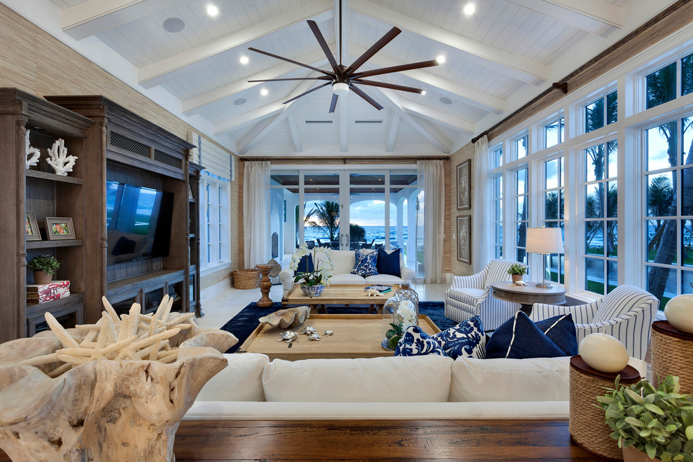 Photo of a large beach style open concept family room in Miami with a built-in media wall, beige walls and limestone floors.