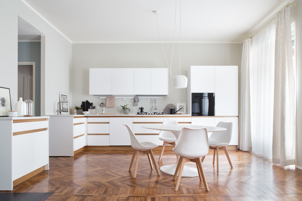 Photo of a mid-sized scandinavian l-shaped eat-in kitchen in Milan with medium hardwood floors, flat-panel cabinets, white cabinets, black appliances, no island and brown floor.