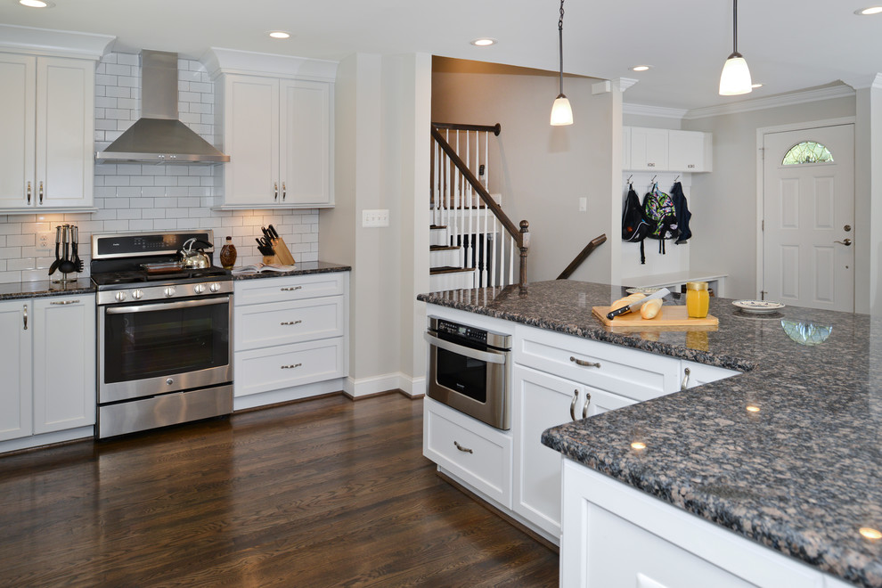 Photo of a mid-sized modern l-shaped eat-in kitchen in DC Metro with flat-panel cabinets, white cabinets, zinc benchtops, white splashback, stainless steel appliances, with island, brown floor and black benchtop.