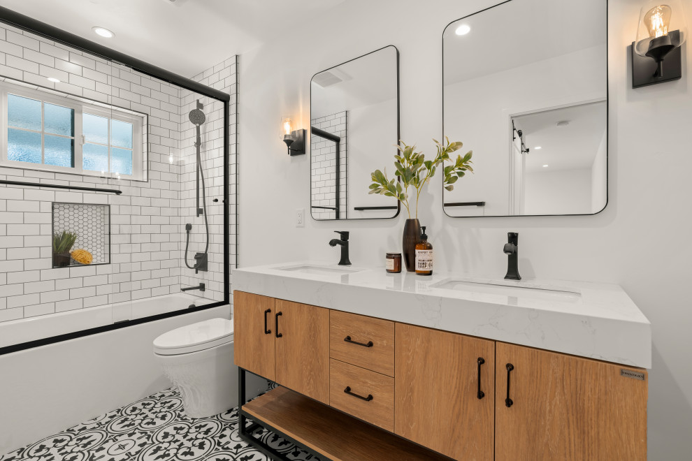 Large contemporary master bathroom in San Francisco with furniture-like cabinets, brown cabinets, an alcove tub, a shower/bathtub combo, a one-piece toilet, black and white tile, porcelain tile, white walls, cement tiles, an undermount sink, solid surface benchtops, multi-coloured floor, a sliding shower screen, white benchtops, a niche, a double vanity and a freestanding vanity.