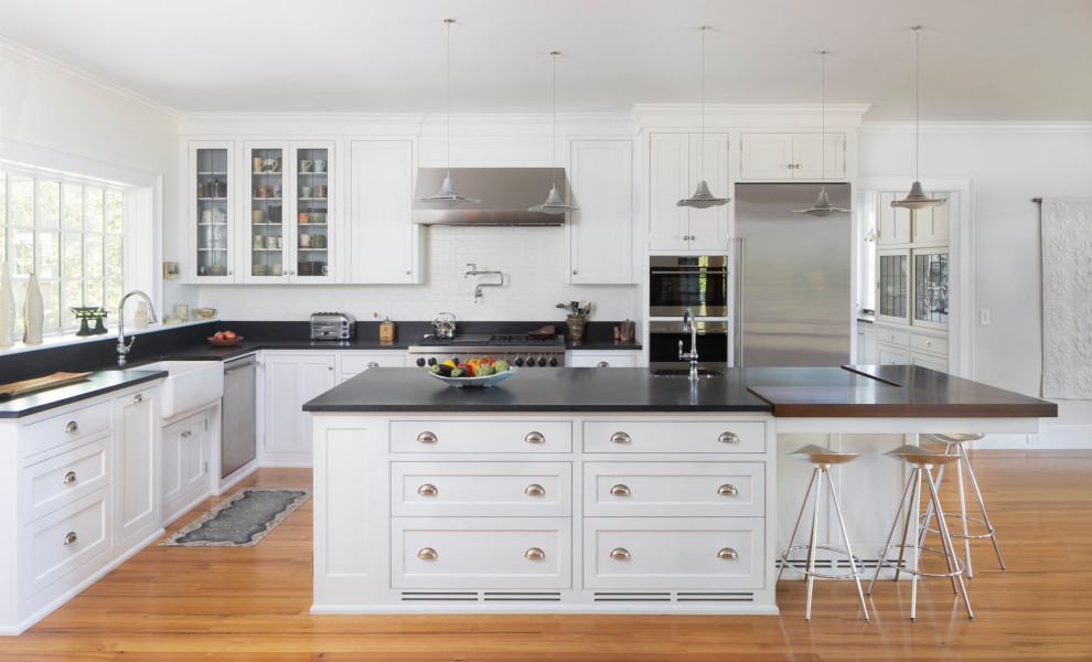 Design ideas for a large country u-shaped kitchen in Providence with a farmhouse sink, recessed-panel cabinets, white cabinets, granite benchtops, white splashback, stainless steel appliances, light hardwood floors, with island and black benchtop.